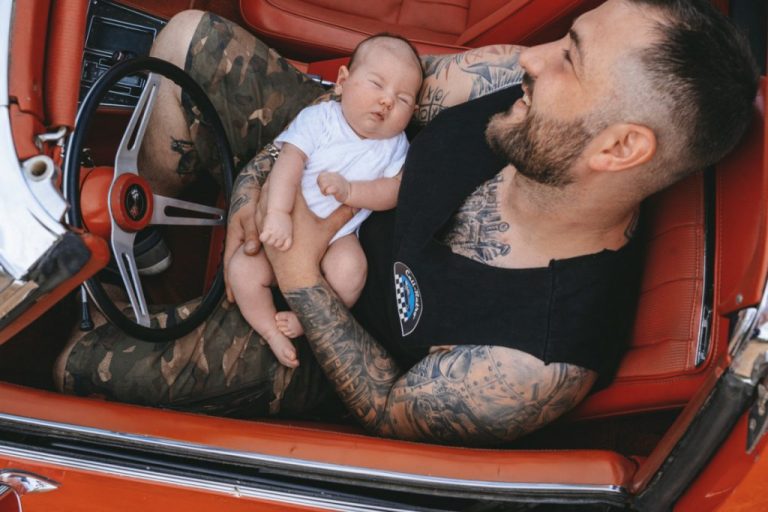 Père tatoué avec son bébé au volant d'une corvette rouge
